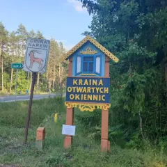 Drewniana tablica wita w Krainie Otwartych Okiennic. Obok znak Gminy Narew.