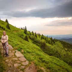 Kobieta na szlaku, zastanawia się, ile się idzie na Śnieżkę. Piękny widok na góry i lasy.