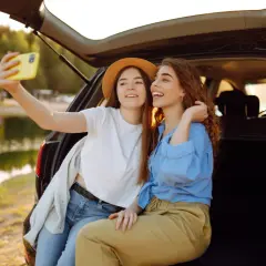 Dwie przyjaciółki robią sobie selfie przy samochodzie nad jeziorem. Idealny weekend z przyjaciółką!