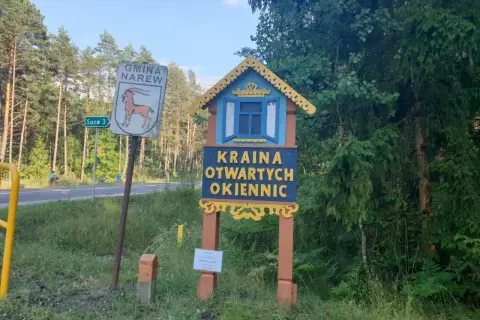 Drewniana tablica wita w Krainie Otwartych Okiennic. Obok znak Gminy Narew.
