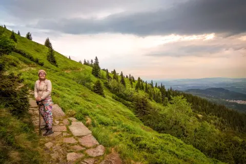 Kobieta na szlaku, zastanawia się, ile się idzie na Śnieżkę. Piękny widok na góry i lasy.