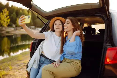 Dwie przyjaciółki robią sobie selfie przy samochodzie nad jeziorem. Idealny weekend z przyjaciółką!